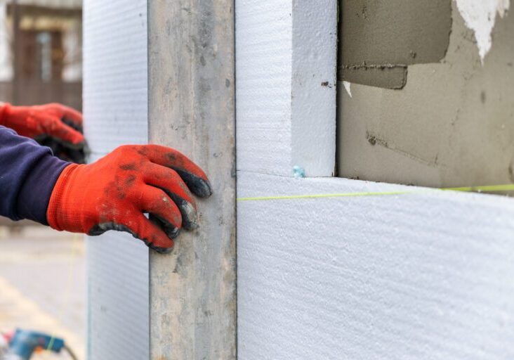 Construction worker installing styrofoam insulation sheets on house facade wall for thermal protection.